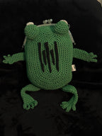 Top-down view of handmade green crochet frog bag with vertical black embroidered scars and metal kiss-lock clasp