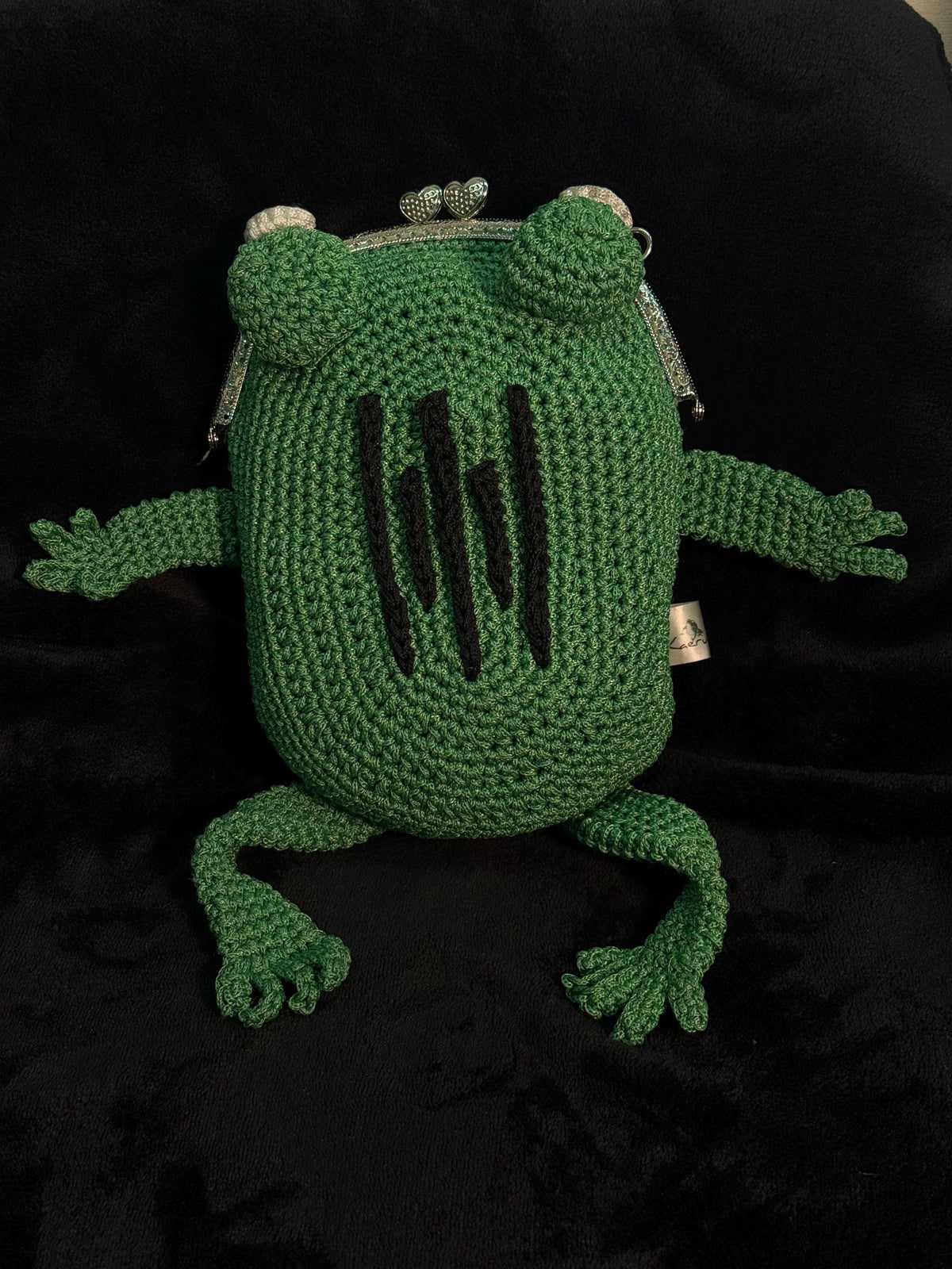 Top-down view of handmade green crochet frog bag with vertical black embroidered scars and metal kiss-lock clasp