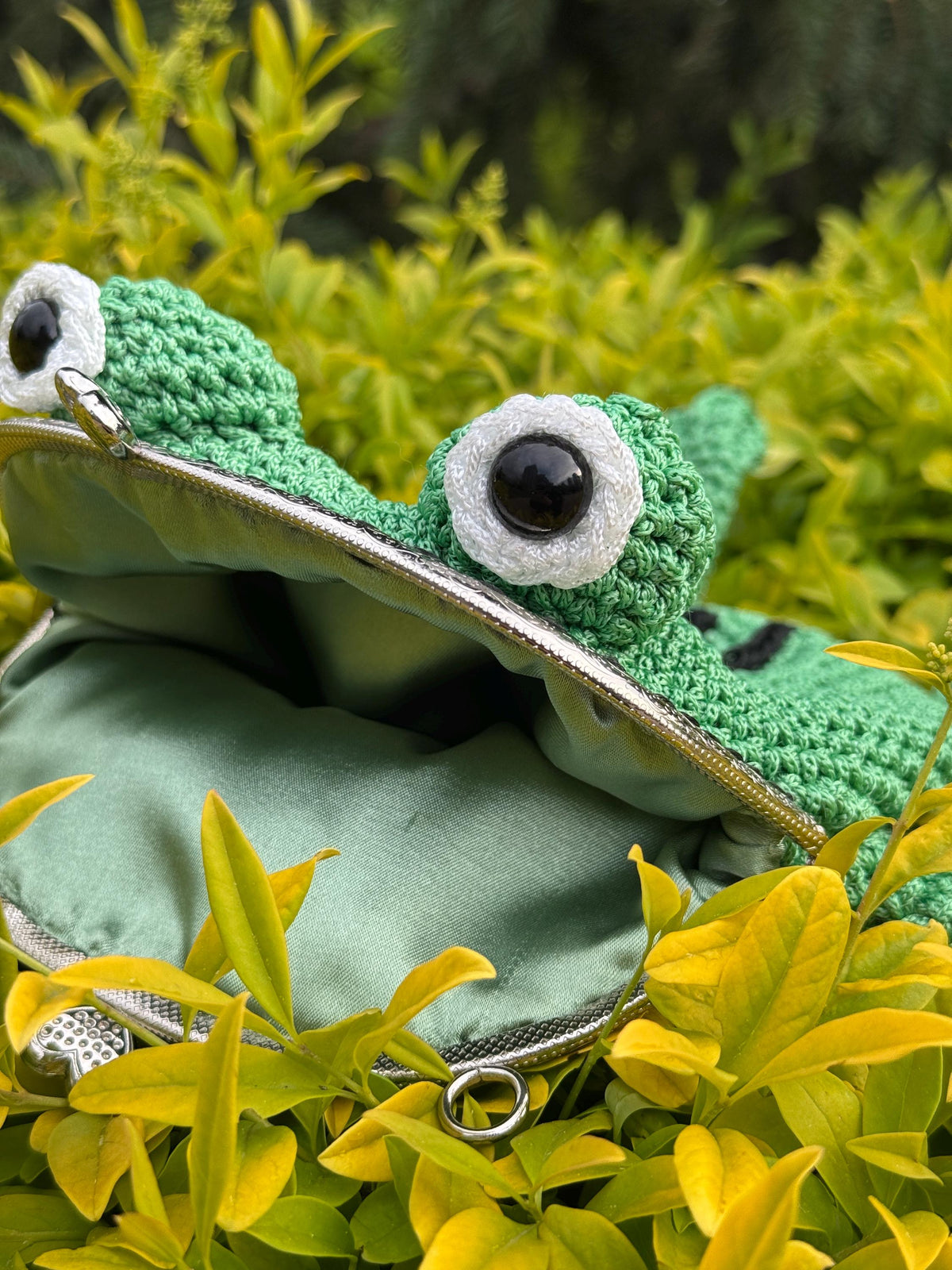 Handmade frog purse among green leaves with eyes looking forward