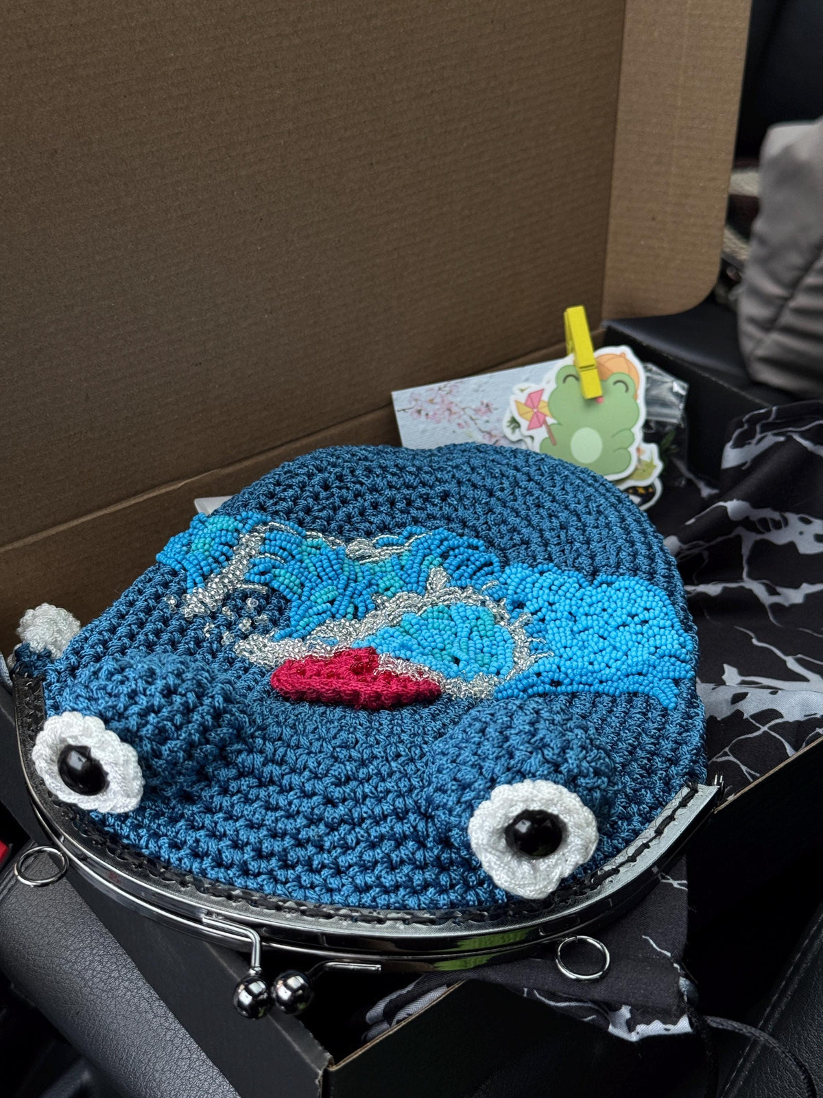 Blue crochet frog bag with wave and red sun embroidery, neatly packed in a box with branded card and sticker