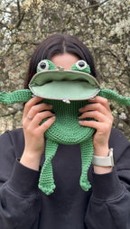 Person playfully holding green frog bag in front of face with hoodie
