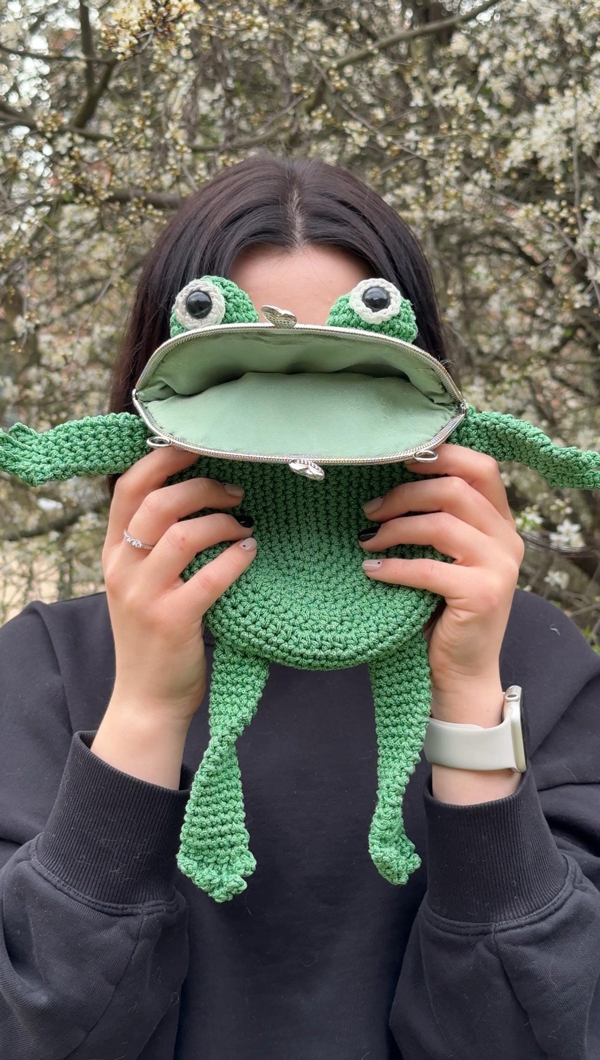 Person playfully holding green frog bag in front of face with hoodie