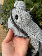 Hand holding a gray crochet frog bag with an open metal clasp, showing the gray cotton lining inside