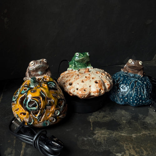 Handmade ceramic frog night lights with textured glazed surfaces on a dark background